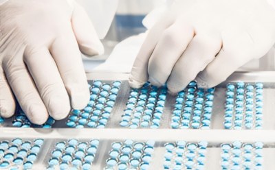 A pair of hands sorting or inspecting blue pills organized in rows on a white tray.