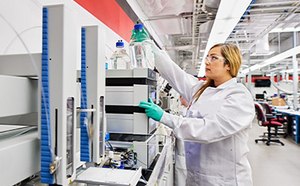 The cover image for the webinar on 'Practical Aspects of HPLC Method Development and LC-Troubleshooting,' featuring a female lab chemist in a laboratory setting. Adorned in green gloves, lab goggles, and a white lab coat, she is actively engaged in an instrument operation.