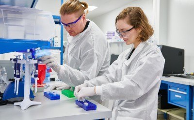 Two laboratory technicians in white coats working at a lab bench, using scientific equipment and preparing samples. Two laboratory technicians in white coats working at a lab bench, using scientific equipment and preparing samples.