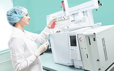 > Female scientific researcher with lab coat, gloves and hair protection placing vial flask in Gas Chromatography instrument > Female scientific researcher with lab coat, gloves and hair protection placing vial flask in Gas Chromatography instrument