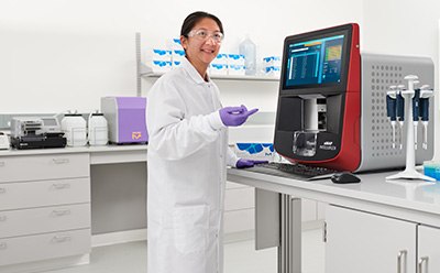 Female scientist in a lab with white coat, goggles, and gloves standing in front of a bench pointing to an xMAP® INTELLIFLEX® instrument that has pipettes and MIILIPLEX® multiplex immunoassay kits next to it. Female scientist in a lab with white coat, goggles, and gloves standing in front of a bench pointing to an xMAP® INTELLIFLEX® instrument that has pipettes and MIILIPLEX® multiplex immunoassay kits next to it.