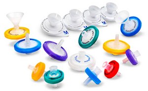 An assortment of Millex<sup>®</sup> syringe filters in various colors and sizes, displayed against a white background. These filters represent a range of small-volume filtration options for laboratory use. The filters come in different colors such as blue, green, yellow, purple, and red, indicating different filter types or pore sizes. Each filter has a circular shape with a conical funnel-like structure on top for attaching to a syringe. The central part of the filters is white with labeling that includes the brand name “Millex®”. Some filters have a transparent top section while others are opaque. There is also one funnel accessory included in the image which is used to assist with pouring liquids into the filter. These filters set the standard in small-volume filtration (1-200 mL), and their unsurpassed consistency in sample preparation has led to the development of many methods specifying their use.