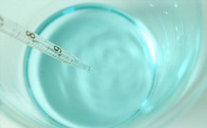 A thermometer measuring the temperature of a clear blue liquid in a glass container.