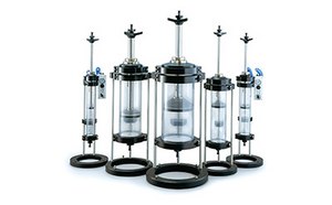 A set of five chromatography columns with varying heights, each featuring a clear middle section, black bases and tops, and some with blue valves. 