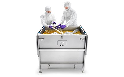 Two people in protective lab attire are interacting with the contents of a large metal container. The container has latches on the side, indicating it may has a lid. Two people in protective lab attire are interacting with the contents of a large metal container. The container has latches on the side, indicating it may has a lid.