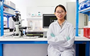 Scientist standing and holding a box of MILLIPLEX® multiplexing biomarker assay reagents next to a Luminex® instrument with an SMCxPRO® ultrasensitive immunoassay instrument on a bench in the background