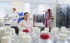 One male and one female scientist working in an analytical development lab for biologics preparing and analyzing samples with many bottles with white and red caps.