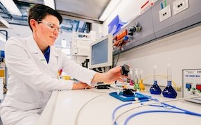 Scientist in a lab, in front of a monitor, using some test tubes to run experiments Scientist in a lab, in front of a monitor, using some test tubes to run experiments