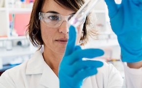 Scientist in a lab carefully looking at a test tube that she is holding in her hands Scientist in a lab carefully looking at a test tube that she is holding in her hands