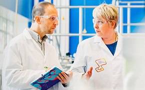 One scientist explaining new innovation to another scientist in front of a blue window