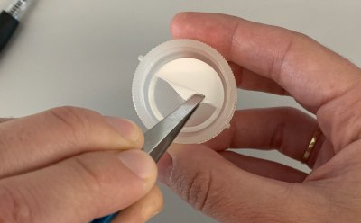 Swinnex<sup>®</sup> Filter Placement Photograph of a person’s hands using forceps to place the cut disc filter