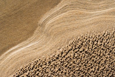 A close-up view of a sand, featuring textured patterns of wet and dry sand, with gentle waves creating smooth lines on the surface A close-up view of a sand, featuring textured patterns of wet and dry sand, with gentle waves creating smooth lines on the surface